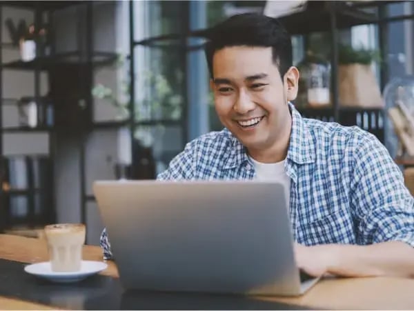 Smiling young entrepreneur using a  laptop at a café, researching SME business financing and loan options.